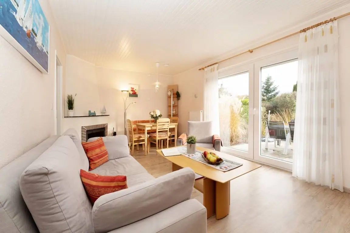 Helles Wohnzimmer mit Sofa, Sessel, Couchtisch und Terrassentür